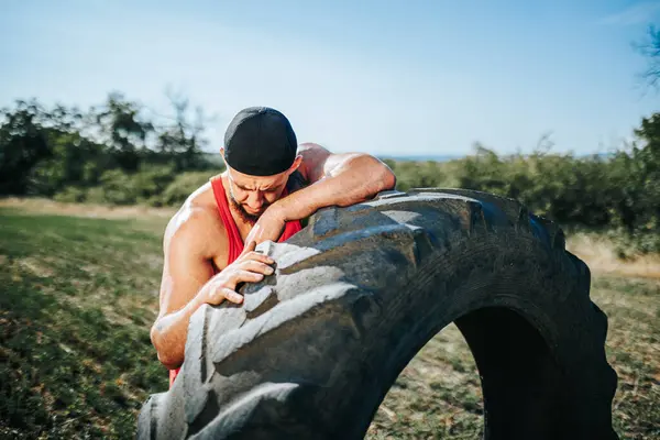 stock image In this portrait, a tired and worn-out muscular man is seen resting after a grueling crossfit training outdoors. He leans on the tire, showcasing the effort and dedication he puts into his athletic