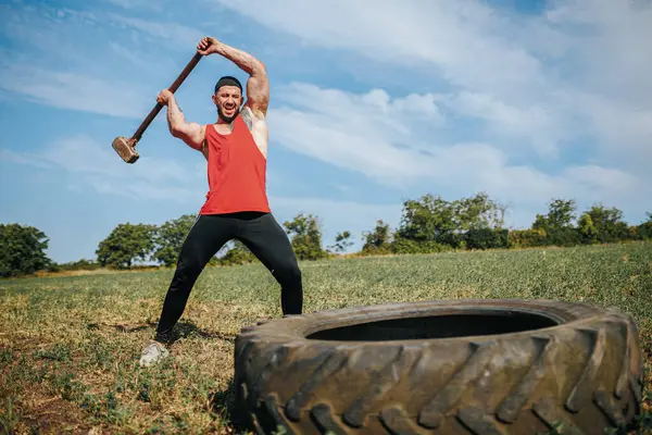 stock image Outdoor Fitness Muscular Man Performing Strength Training, Smashing Rubber Tire at Crossfit Session. Cross fit Challenge Muscular Man Hits Tire with Sledgehammer in Outdoor Training