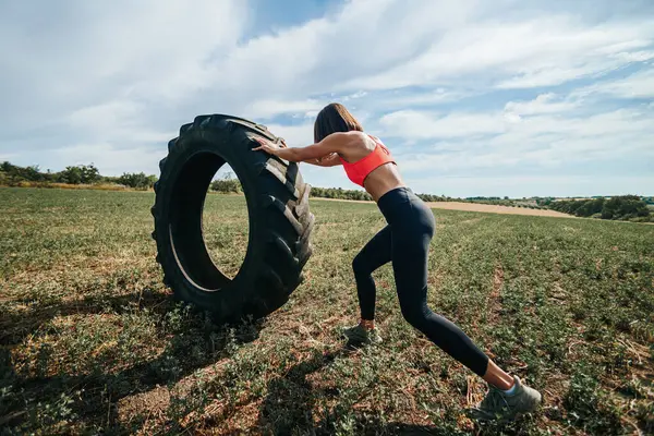 stock image CrossFit fitness woman displaying determination and effort while lifting a wheel outdoors. Outdoor Cross Fit Routine Strong Woman Lifting a Wheel with Determination