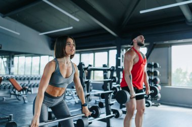 İki genç Kafkasyalı, bir erkek ve bir kadın, spor salonunda yan yana halter çalışırlar, fitness hedeflerine odaklanırlar..