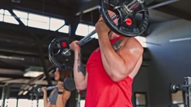 Bir çift fitness meraklısı, bir Amerikalı erkek ve bir İspanyol kadın spor yaparken kas güçlerini sergiliyorlar..