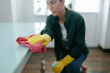Sarı eldivenli bir ev hanımı, kendini mutfak masasını temizlemeye adamış, temiz ve düzenli bir ev halkının sorumluluklarını temsil ediyor..