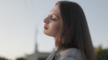 Açık havada günbatımının tadını çıkaran esmer bir kadının yakın çekimi, yumuşak altın ışığın altında parlayan doğal güzelliği..