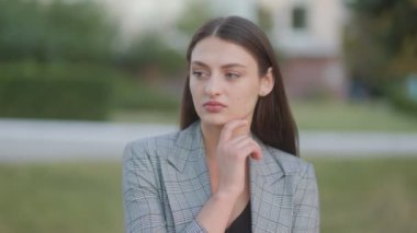 Açık havada esmer bir kadın, şüpheli bir ifadeyle kameraya bakıyor. Yüzü, doğal bir arka plana karşı ince bir şüphe gösteriyor..