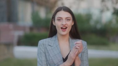 Genç, esmer bir kadın, parlak ve mutlu bir gülümsemeyle doğrudan kameraya bakar. Yüzündeki ifade neşe ve memnuniyet saçıyor, dışarıda gerçek bir mutluluk anı yakalıyor..