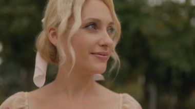 Gülümseyen, orta yaşlı, orta yaşlı bir kadın dışarıda doğal ortamda duruyor. Rahatlamış ve mutluluk saçıyor..