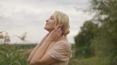 Sarışın, orta yaşlı bir kadının doğal bir ortamda gülümsediği ve güneş ışığının yüzünü çerçevelediği samimi bir vesikalık..