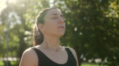 Güneşli bir günde parkta spor yaptıktan sonra huzur içinde dinlenen esmer saçlı genç beyaz bir kadın, sakin, rahat bir açık hava portresiyle yakalandı..