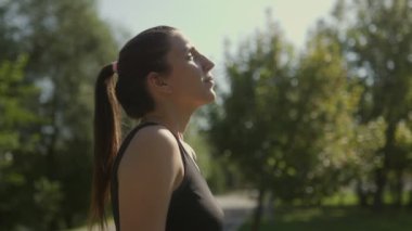 Genç ve zinde bir esmer kadın, güneşli bir günde, bu rahat portrede enerji ve canlılık saçarak parkta yaptığı egzersizden sonra dinleniyor..