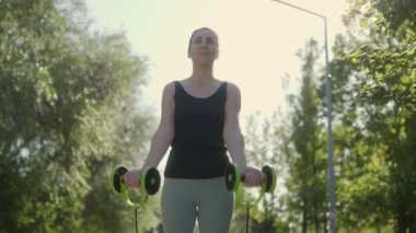 Kendinden emin ve atletik, genç esmer bir kadın güneşli bir günde parkta spor yapmak için direniş bantları kullanıyor..