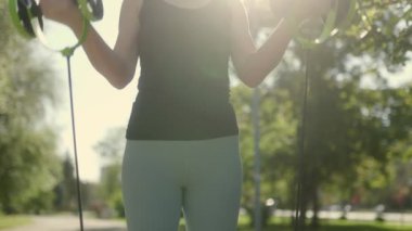 Parkta direniş bandı fitness antrenmanına katılan tanınmamış bir kadın. Fiziksel hedeflerine odaklanırken güneşli günün tadını çıkarıyor. Kapat.