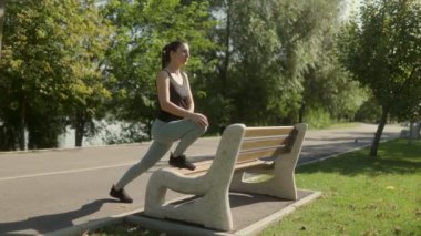 Esmer bir kadın güneşli bir günde parkta antrenman yapıyor. Güneş ışığının tadını çıkarırken kendine güven ve canlılık saçarak fiziksel egzersizler yapıyor..