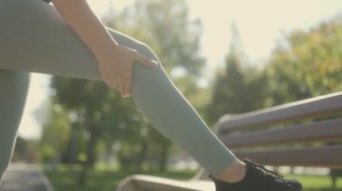 Sportif genç bir kadın, güneşli bir parkta jimnastik yaparken diz ağrısıyla karşılaşır. Dizindeki rahatsızlıktan dolayı antrenman seansını durdurur..