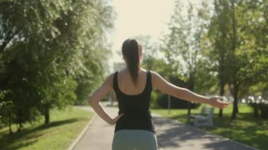 Genç, esmer, beyaz bir kadın güneşli bir parkta spor yapıyor. Eğitimdeyken açık havayı seviyor, sağlıklı ve aktif bir yaşam tarzını kucaklıyor..