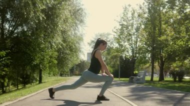Genç atletik kadın güneşli bir günde parkta fiziksel egzersiz yapıyor. Odaklanmış, enerjik ve dışarıdaki fitness hedeflerine kendini adamıştı..