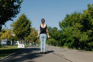 Aktif bir genç kadın parkta direniş bandı eğitimi alıyor. Atletik egzersiz rutini, güneşli gökyüzünün altında sağlıklı ve kendinden emin bir yaşam tarzını kucaklıyor. arka plan