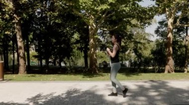 Genç bir kadın parktaki jimnastik egzersizlerini bitirdikten sonra şişeden su içer ve güneş ışığında enerjisini tazeler..