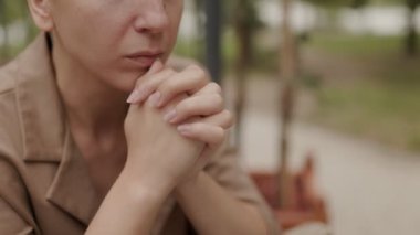 Takım elbiseli beyaz esmer bir kadın terasta dizüstü bilgisayarının yanında oturuyor, derin düşüncelere dalmış, ciddi ve konsantre bir ifadeyle uzaktan çalışıyor..