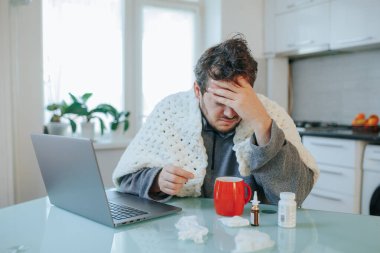 Frijit Freelance Tousled saçlı adam baş ağrısı, grip, yorgana sarılı, laptopun yanında, bir ev ofisinin soğuk pençelerinde.
