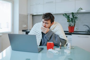 Genç, sakallı bir Kafkasyalı. Gribi evden yönetiyor. Mutfak sandalyesine oturmuş, yorgana sarılmış ve dizüstü bilgisayarda çalışan birey mevsimsel hastalıklarla baş ederken resmedilmiş.