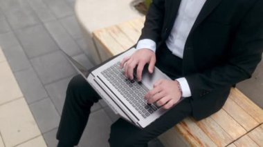 Siyah bir duvara karşı sakallı ve gözlüklü, takım elbiseli genç bir iş adamı. Laptop kullanıyor. 