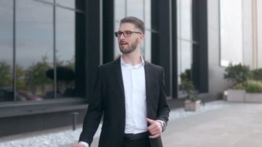 Siyah bir duvara karşı sakallı ve gözlüklü, takım elbiseli genç bir iş adamı. Sokakta dans ediyor. 