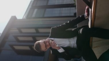 Siyah bir duvara karşı sakallı ve gözlüklü, takım elbiseli genç bir iş adamı. Laptop kullanıyor ve dışarıda öğle yemeği yiyor.