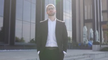 Siyah bir duvara karşı sakallı ve gözlüklü, takım elbiseli genç bir iş adamı. Düşünceli bir şekilde yukarı bakıyor.