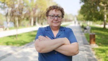 Açık havada kollarını kavuşturmuş yaşlı bir kadının portresi.