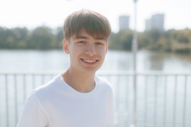 Beyaz tişörtlü neşeli bir genç çocuk dışarıda dikilirken kameraya ışık tutuyor. Rahatlamış ve arkadaş canlısı tavrı ergenliğin tasasız özünü yakalıyor..