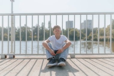 Rahat genç bir çocuk rahat bir şekilde oturur, akıllı telefonunu tutarken gülümser, internette gezinirken ve dijital dünyayla bağlantıda kalırken özgürlüğünün kaygısız anının tadını çıkarır..