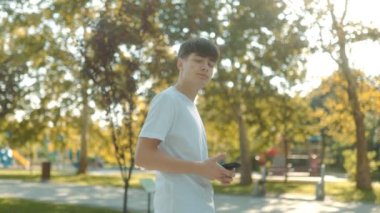 Güneşli bir günde şehir parkında beyaz tişörtlü, akıllı telefonlu genç bir çocuk. Etrafı yeşilliklerle çevrili, gençlik neşesi ve özgürlük yayıyor.