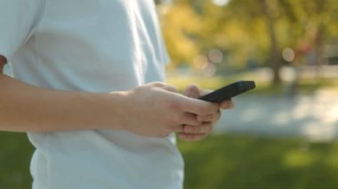 Güneşli bir günde şehir parkında beyaz tişörtlü, akıllı telefonlu genç bir çocuk. Etrafı yeşilliklerle çevrili, gençlik neşesi ve özgürlük yayıyor.