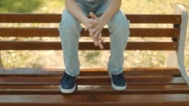 Güneşli bir günde şehir parkında bankta oturan beyaz tişörtlü genç bir çocuk..