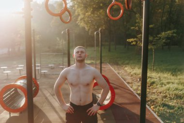 Çıplak gövdeli zinde bir genç adam zorlu bir açık hava antrenmanından sonra kendine güveniyor atletik vücudunu gösteriyor ve sağlıklı kalmaya kararlı..