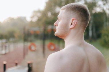 Çıplak gövdeli genç bir erkek sporcunun arka görüntüsü, yoğun açık hava egzersizleri yapıyor, zayıf, kaslı yapısını ve fitness bağlılığını gösteriyor..