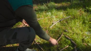 Sessiz bir orman ortamında, bir adam orman zemininde diz çökerek kuru dal ve dallar toplar. Bu sahne hayatta kalma becerilerinin ve doğa keşiflerinin özünü yakalar..