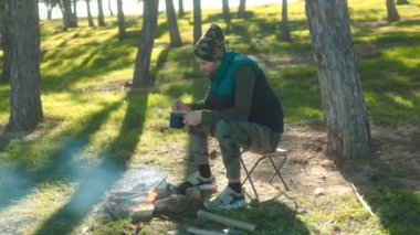 Huzurlu bir ormanda kamp ateşinin yanında çömelmiş bir adam alevlerin üzerinde demlik karıştırıyor. Doğayla çevrili açık hava yemeklerinin sakin ve sade olmasından hoşlanıyor..