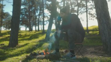 Ormanda bir kamp ateşinin yanında oturan bu adam, doğanın sakin atmosferini kucaklayarak çay molası verir. Onun yansıtıcı ifadesi sakin bir çevreye ekleniyor..