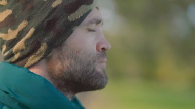 Mavi gözlü, bereli sakallı bir adam, açık havada sakin, yansıtıcı bir anda yakalandı. Onun engebeli görünüşü sakin orman zeminini tamamlıyor..