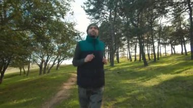 Güneşli bir ormanlık alanda koşan bir adam, doğanın temiz havasını ve dinginliğini kucaklıyor. Sıcak bir şekilde giyinmiş, ormanda kardiyo çalışmasının faydalarından hoşlanıyor..