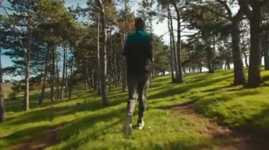 Arkadan görülen bir adam, barışçıl bir orman patikasında kamuflaj pantolonuyla koşuyor, doğanın güzelliğini ve koşusu sırasında etrafındaki sakinliği tamamen kucaklıyor..