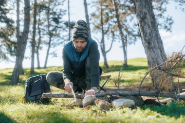 A lone man cuts branches with a manual saw in a quiet, wooded area. His focus on survival skills emphasizes his connection to nature and self-sufficiency. clipart