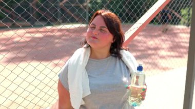 Spor giyimli şişman bir kadın su şişesiyle dışarıda duruyor. Sağlıklı yaşam tarzı kilo vermek için düzenli egzersiz yapmayı içeriyor..