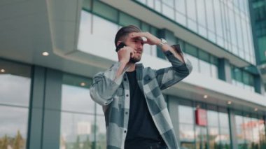 Endişeli ve endişeli bir genç sakallı adam şehir merkezinde telefonla konuşuyor. Sakallı bir erkek dışarıda endişeli bir telefon görüşmesi yapıyor.