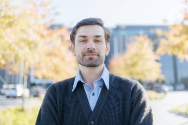 Bir ofis çalışanı açık havada poz veriyor, kendine güvenen bir ifadeyle kameraya bakıyor. Arka plandaki sonbahar yaprakları sıcak ve davetkar bir atmosfer yaratıyor.