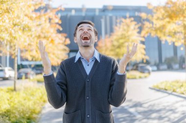 An astonished man in casual clothing looks around in awe, taken aback by something unseen. His facial expression is a mix of surprise and amazement against a busy city backdrop. clipart