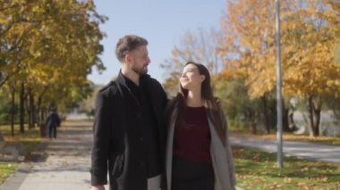 Mutlu bir çift, renkli yapraklarla çevrili bir sonbahar parkında kol kola yürür. Sevgi dolu bakışlarını paylaşıyorlar, doğada birlikte güzel bir anın tadını çıkarıyorlar..