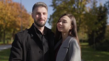 Bir erkek ve kadın, güzel bir sonbahar ortamında kameraya gülümseyerek dışarıda günün tadını çıkarırlar. Çift arasındaki bağ ve aşk bu samimi açık hava portresinde yayılıyor..