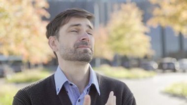 Hüsrana uğramış beyaz yakalı bir işçi, boğulmuş hissediyor, ağaçların sonbahar renklerinde olduğu modern bir binanın yanında duruyor, duygusal yorgunluk anını yakalıyor..